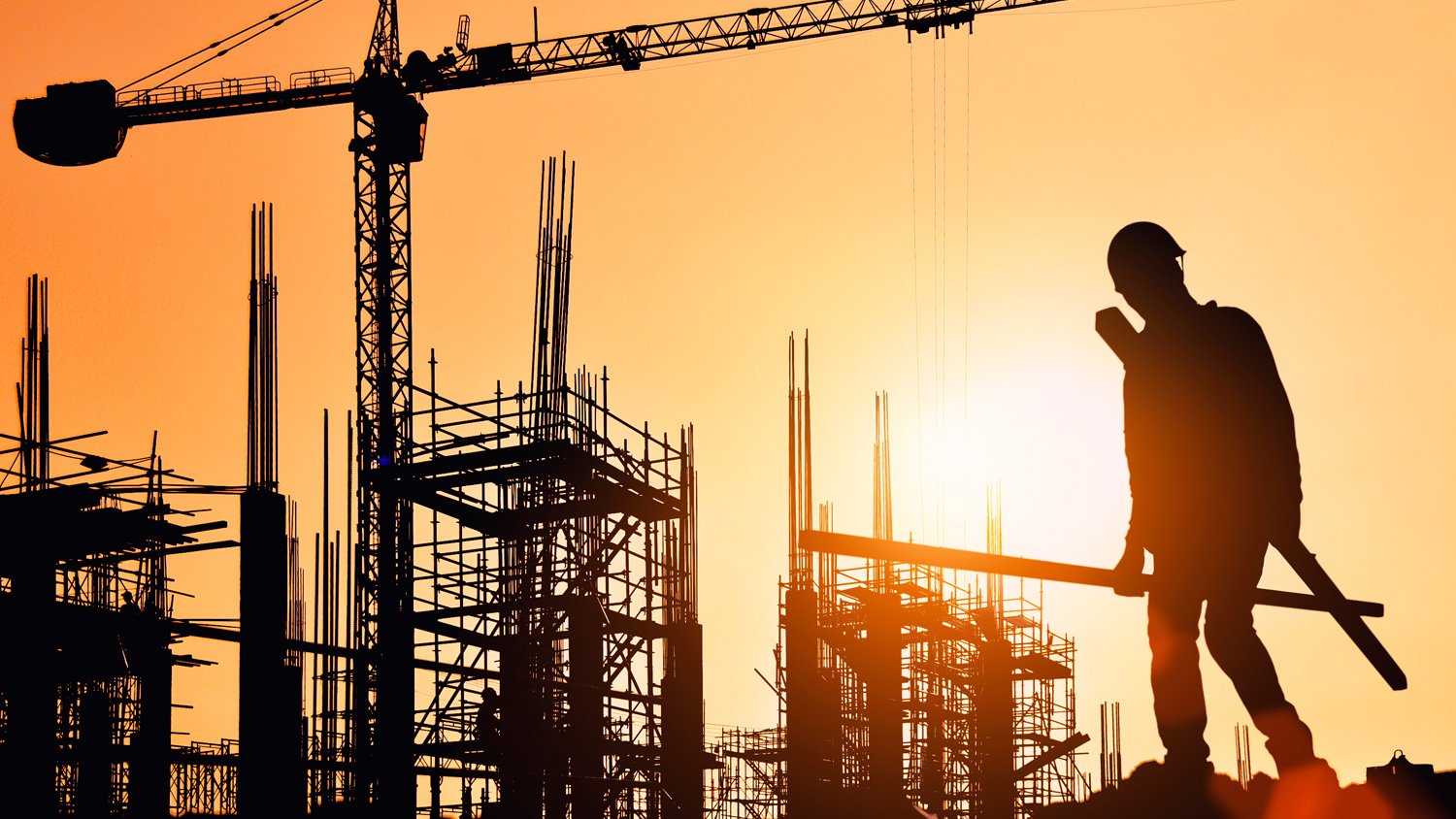 Silueta de un obrero sobre una estructura de concreto al atardecer